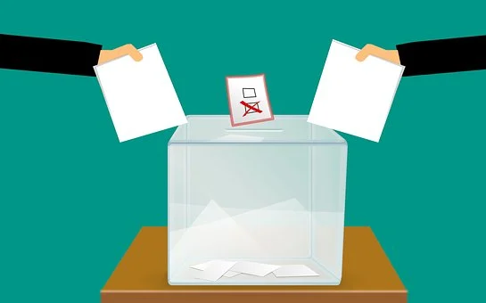 Wahlurne, in der ein Wahlzettel eingeworfen wird